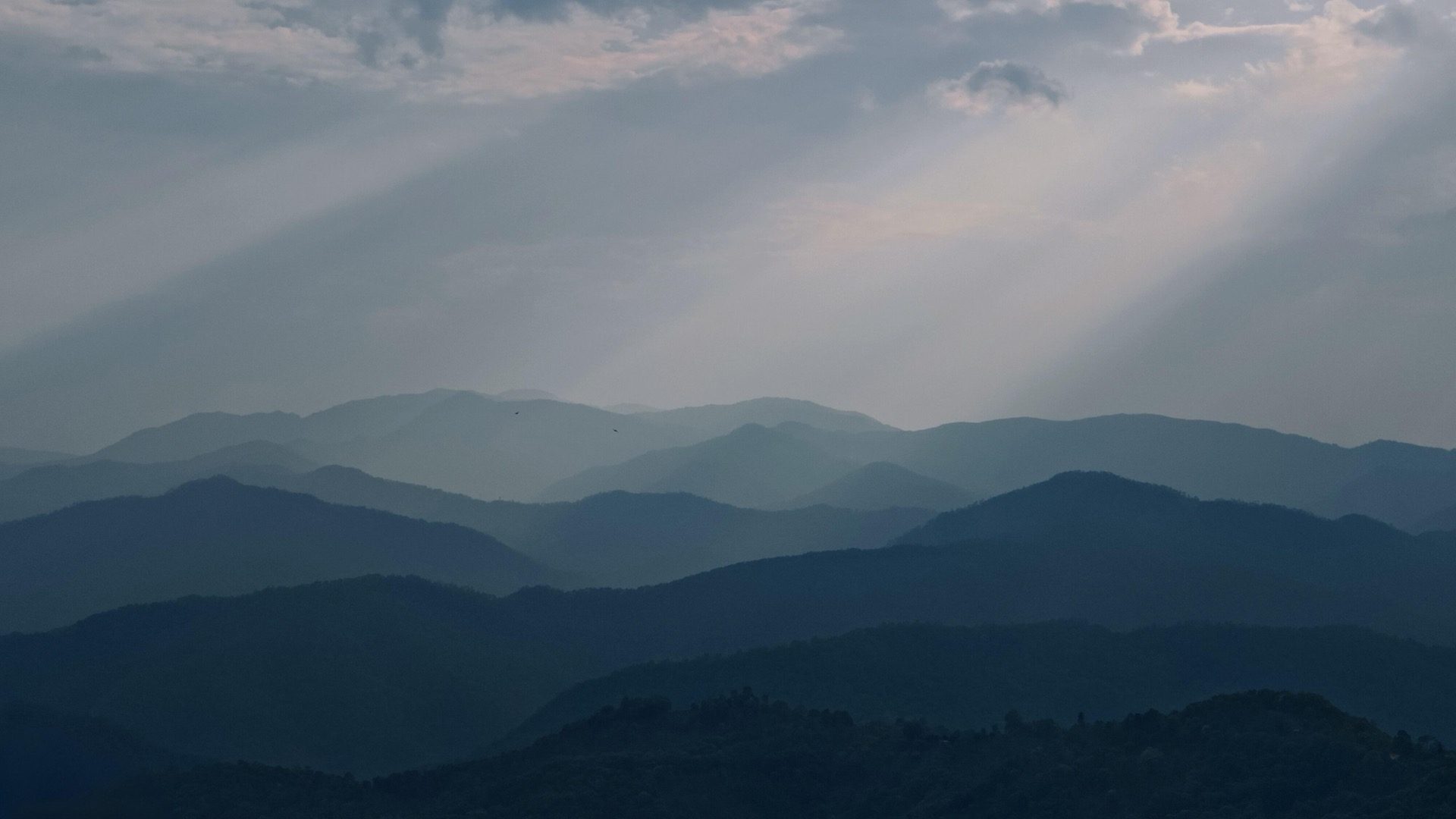 Layered misty mountain ridges with god-rays through the clouds over the Pu'er tea country — Nannuo and Jingmai's UNESCO-listed Pu'er tea ecology